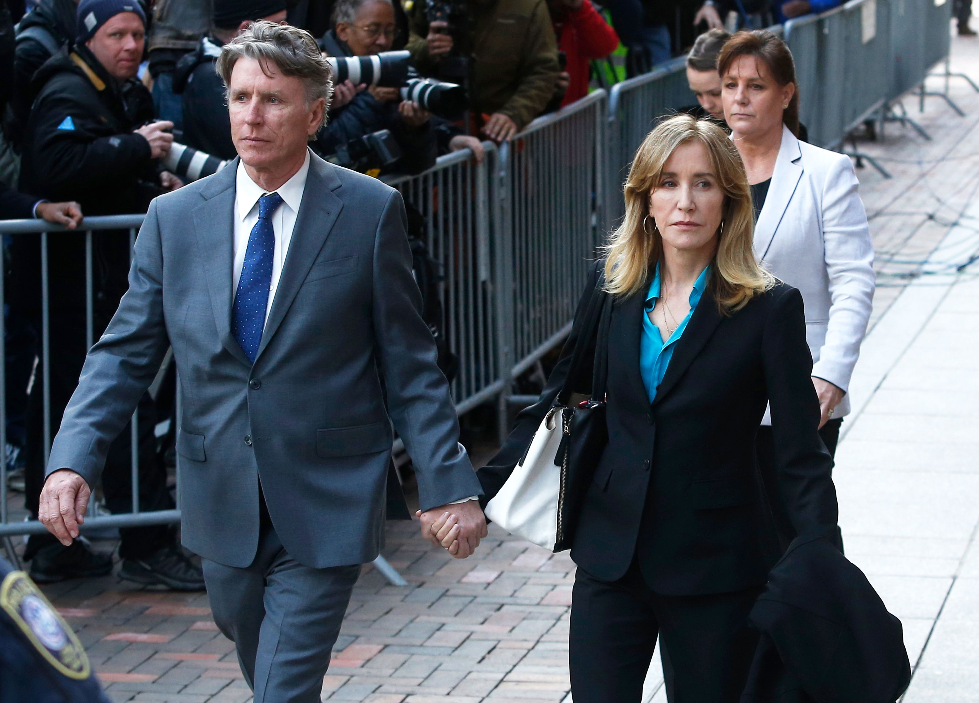 felicity huffman walking on a street outside the courthouse in a black suit