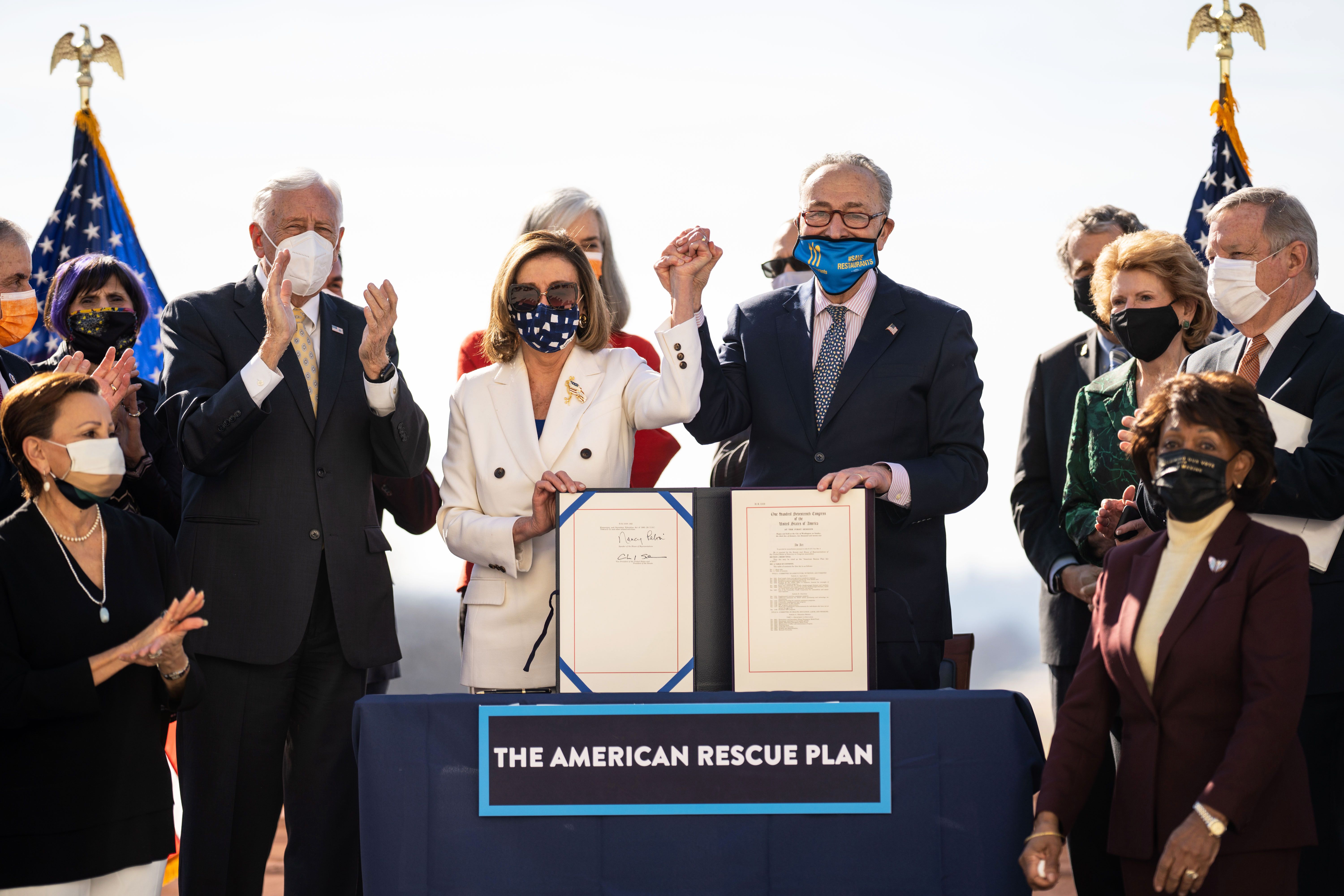 nancy pelosi and chuck schumer holding hands and celebrating the passage of the american rescue plan ac